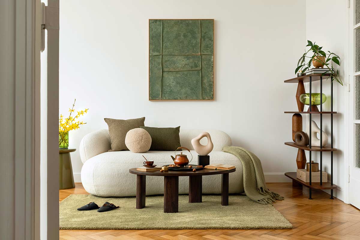 Soggiorno moderno con divano chiaro, tappeto verde salvia, tavolino in legno scuro e dettagli naturali. Atmosfera luminosa e rilassante.