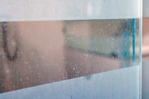 Dettaglio di vetro doccia con aloni di calcare e gocce d’acqua, tipico problema delle superfici non trattate