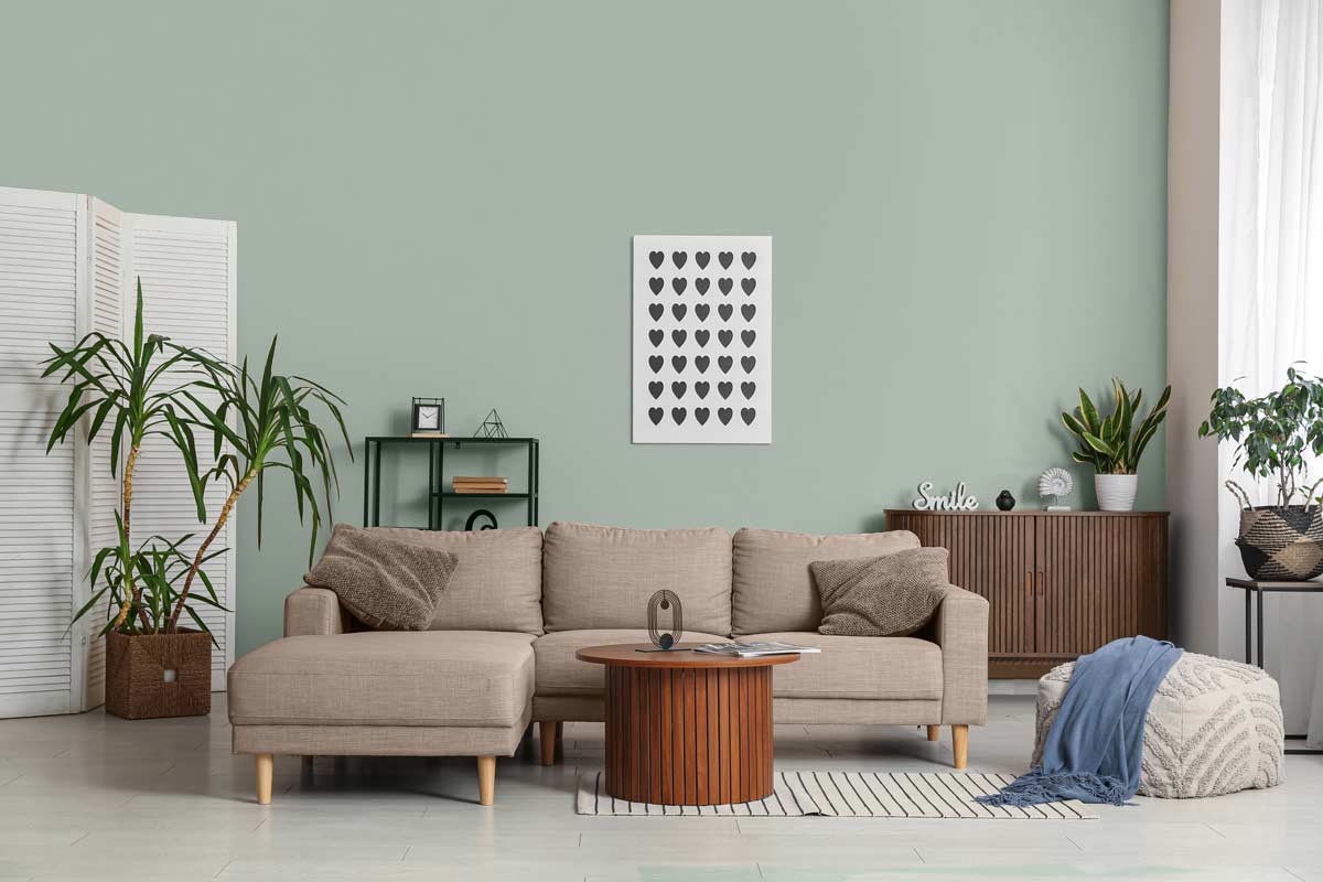 Soggiorno moderno con parete verde salvia, divano beige e mobili in legno, decorato con piante e dettagli naturali.