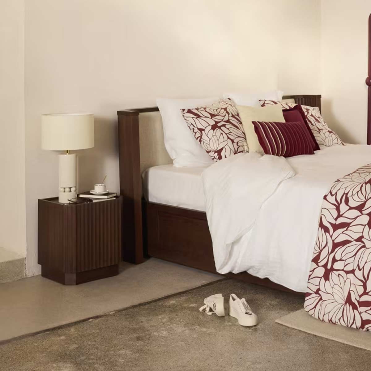 Comodino Bosco di Maisons du Monde accanto a un letto matrimoniale, con lampada e tazza sulla superficie, in una camera dai toni naturali e dettagli in rovere scuro.