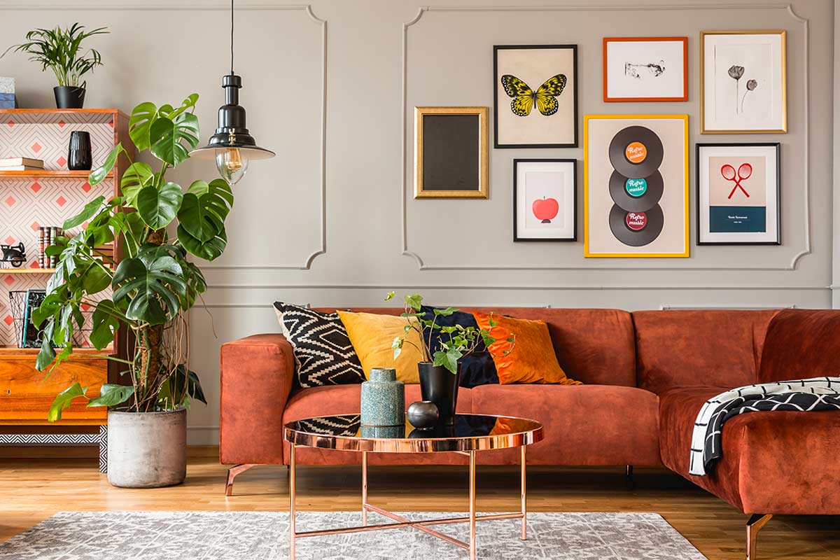 Soggiorno con divano color mattone, piante e galleria a muro di quadri colorati con cornici di diverse dimensioni.