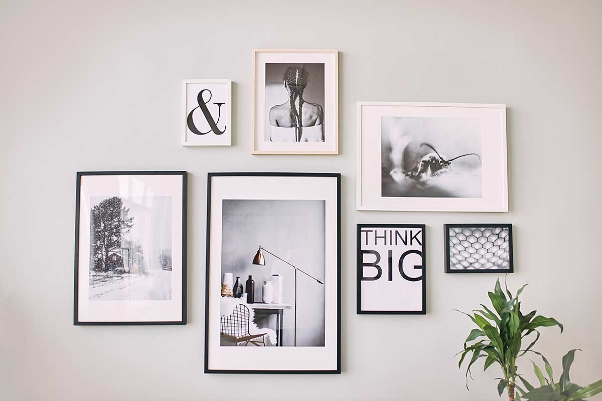 Galleria a muro con cornici di diverse dimensioni disposte in modo armonioso su parete chiara.