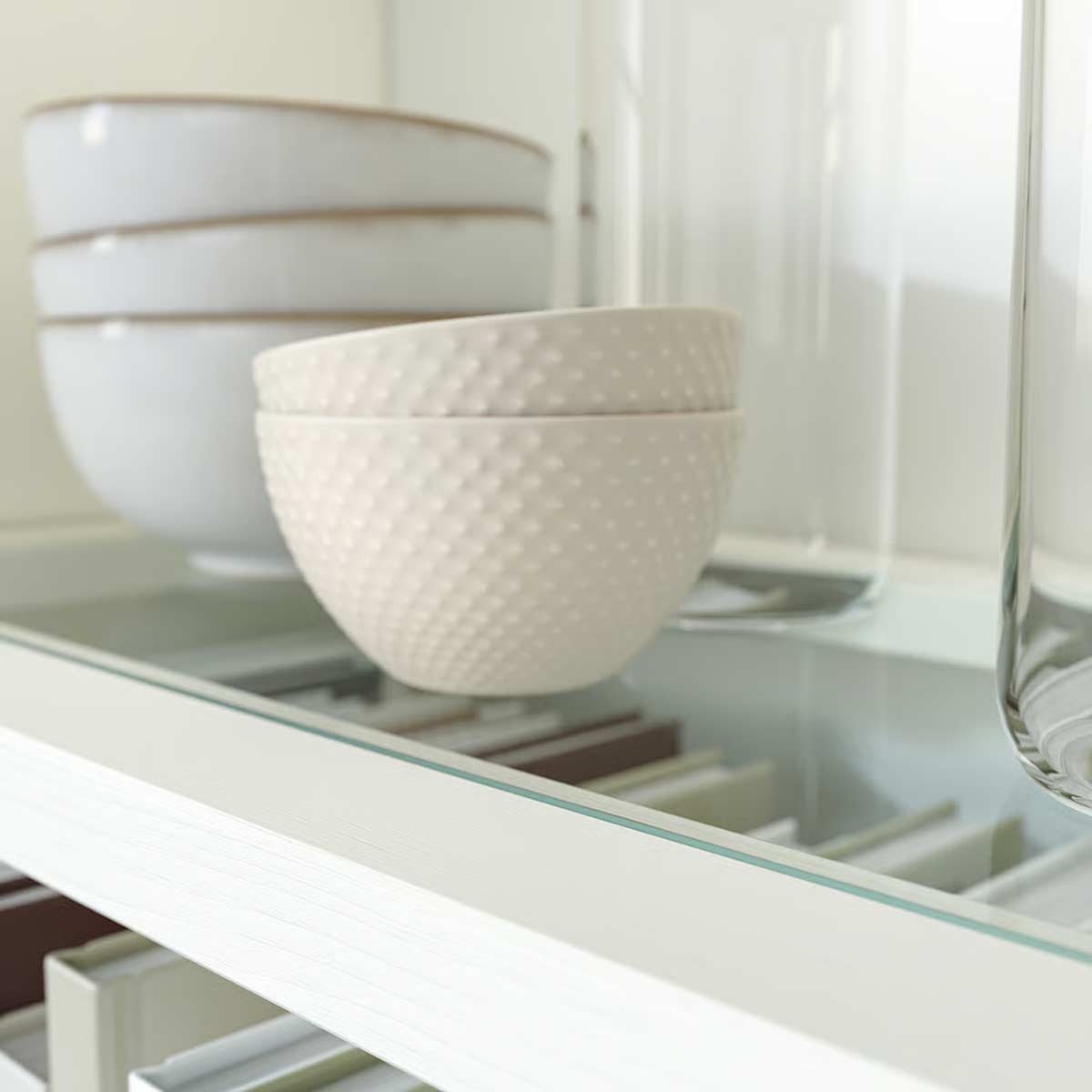 Ripiano in vetro temprato di una credenza Havsta IKEA con ciotole in ceramica e libri ordinati.