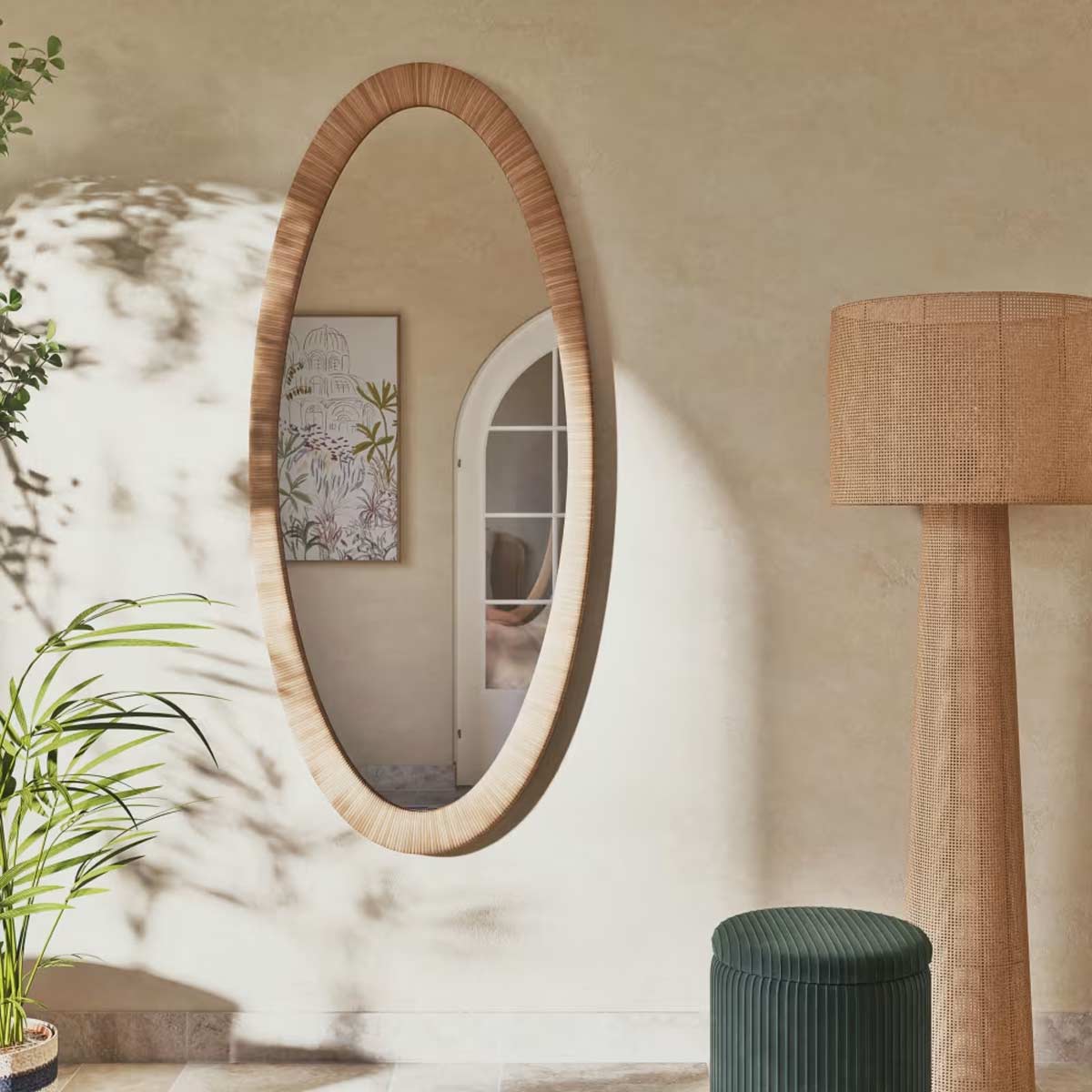 Angolo di soggiorno con specchio ovale, lampada da terra in rattan intrecciato e pouf verde a coste.