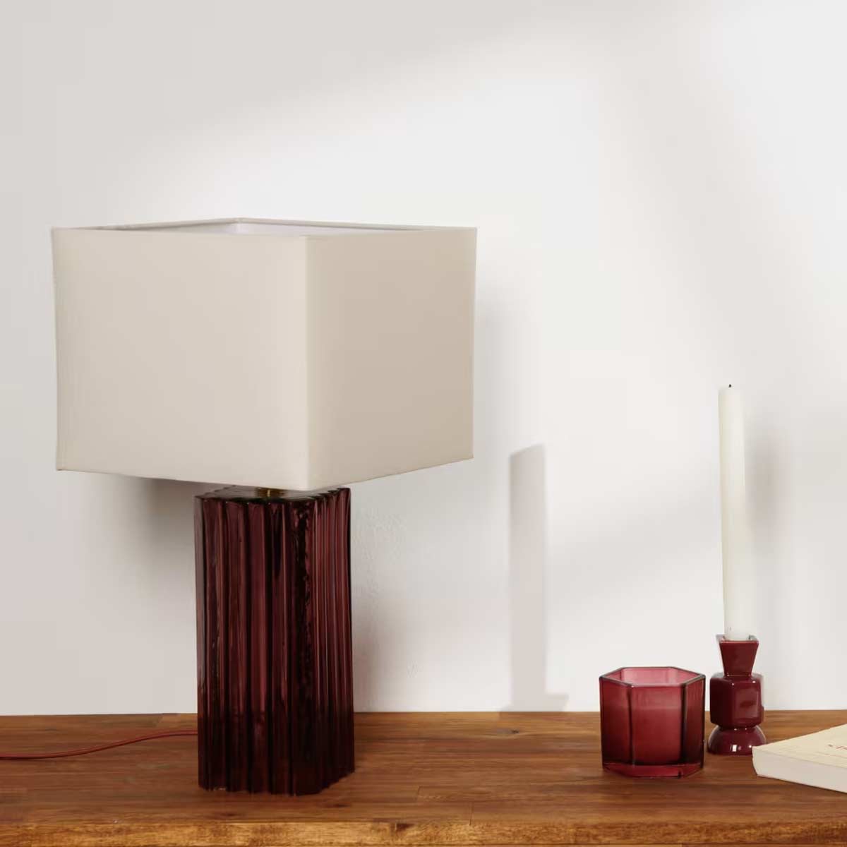Lampada Melone Maisons du Monde con base in vetro bordeaux e paralume crema su tavolo in legno, perfetta per illuminare con stile ambienti moderni e accoglienti