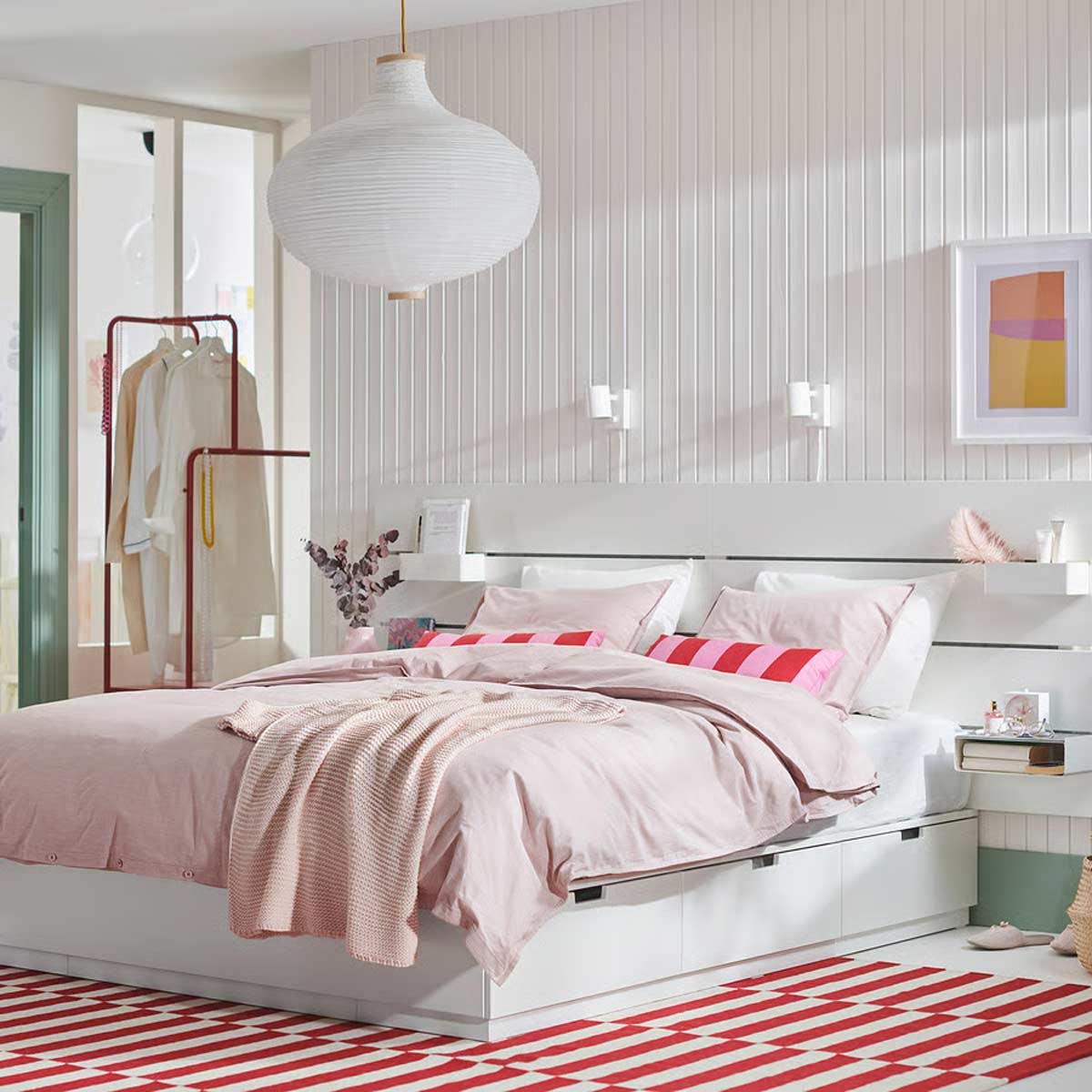 Camera da letto luminosa con letto bianco contenitore, testiera con mensole integrate e biancheria rosa, stile nordico moderno.