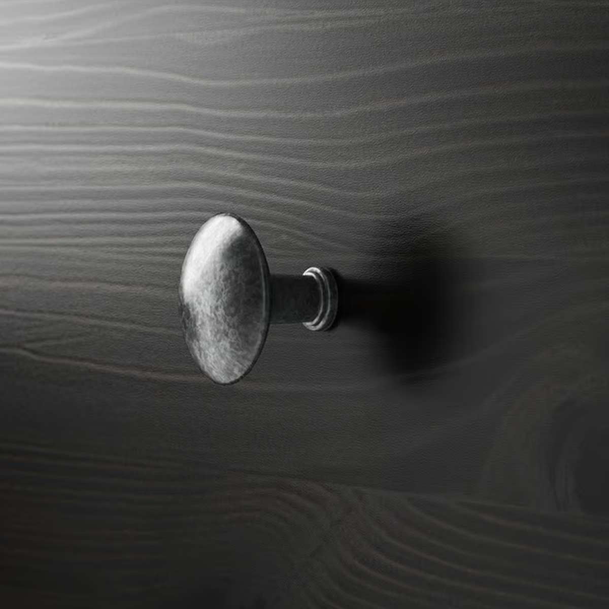 Primo piano di un pomello metallico su anta marrone-nera con venature del legno visibili.