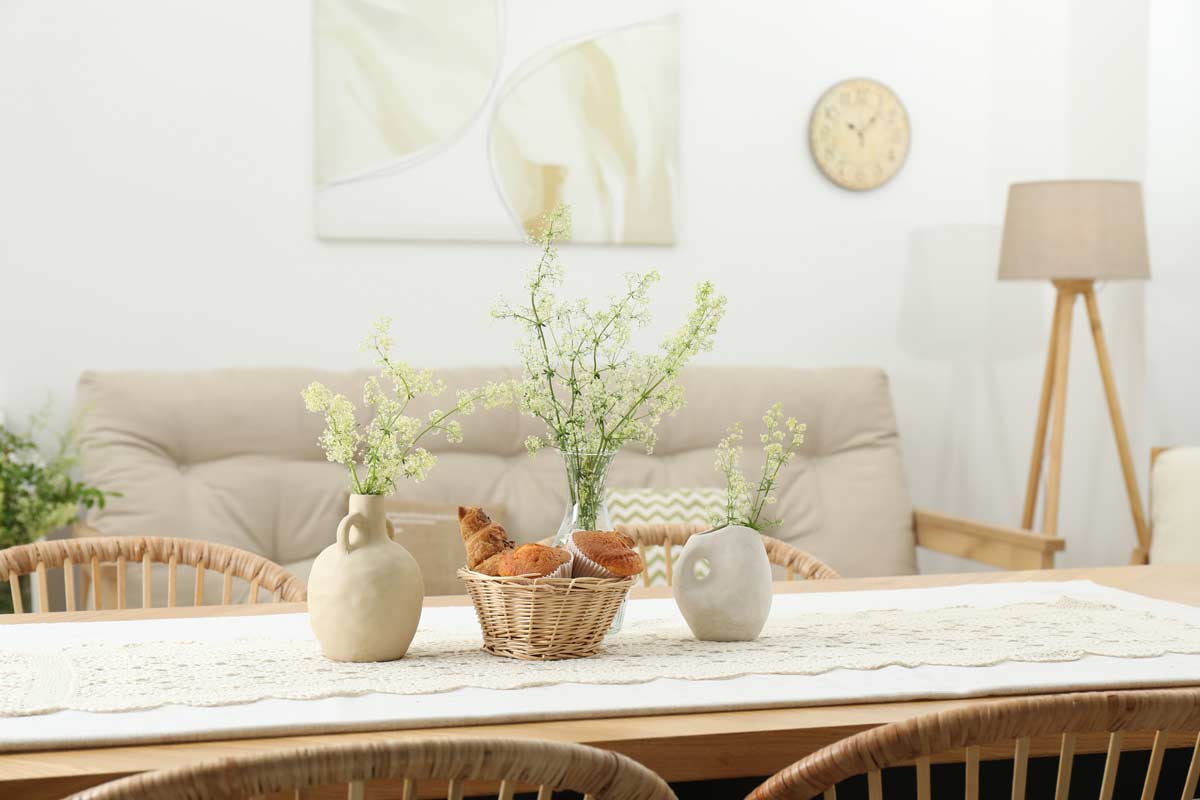 Cesta in fibra naturale con pane su tavolo in legno, circondata da vasi e soggiorno luminoso sullo sfondo