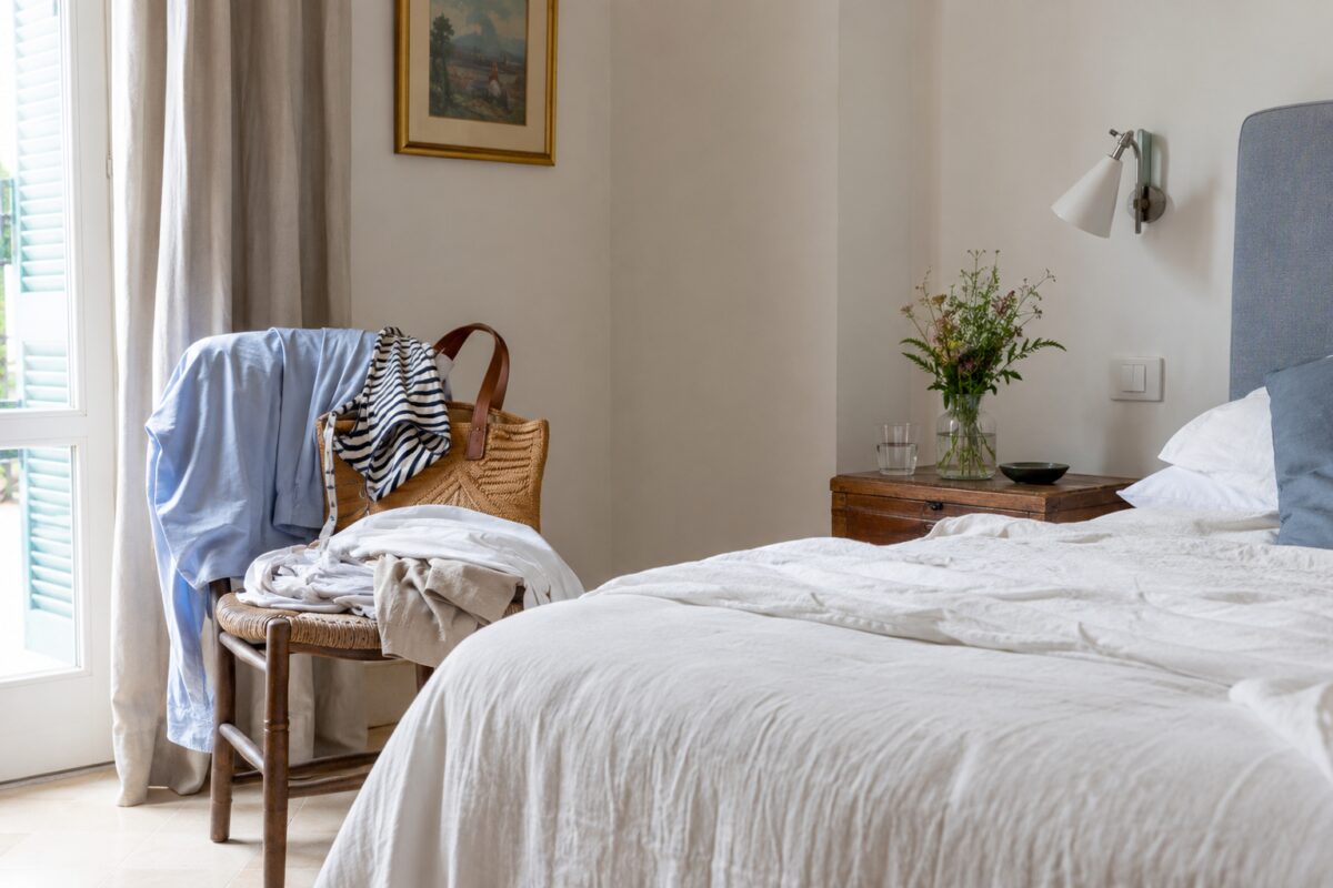 Camera da letto estiva con sedia piena di vestiti vicino al letto