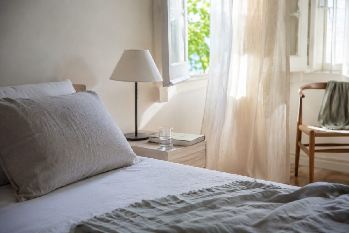 Comodino ordinato e tenda chiara in camera da letto estiva